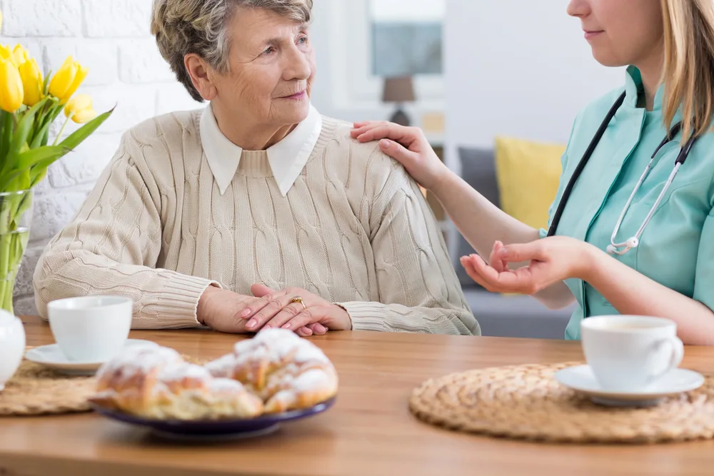 Senior woman getting support from a transitional caregiver over coffee and cake