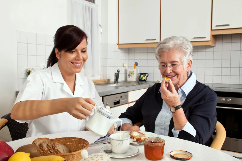 Caregiver feeding a senior woman as part of a transitional care management plan.