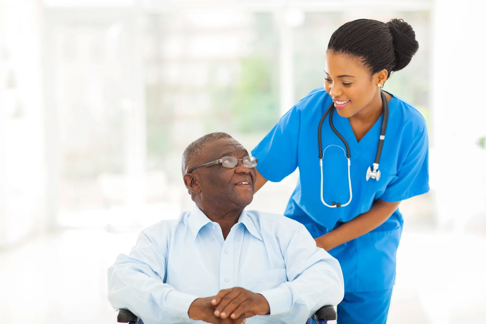 Senior man in a wheelchair talking to a caregiver in a nursing home.