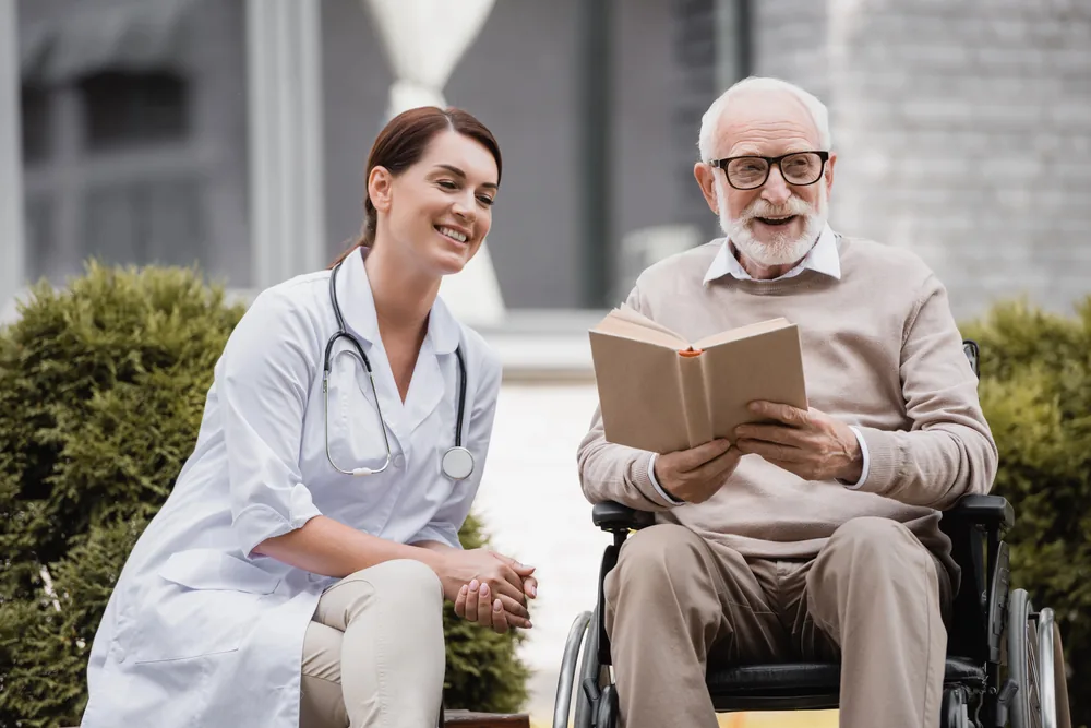 Man in a wheelchair reading outside a nursing home with support from a care manager.