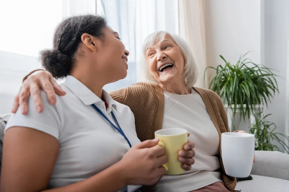 Happy senior woman and caregiver sharing coffee after transitioning to a home.